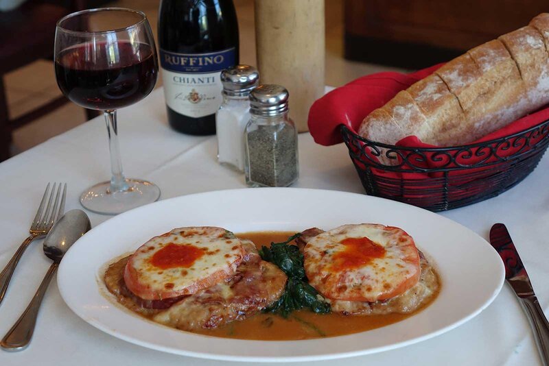 Veal entree with a basket of bread and a glass of red wine