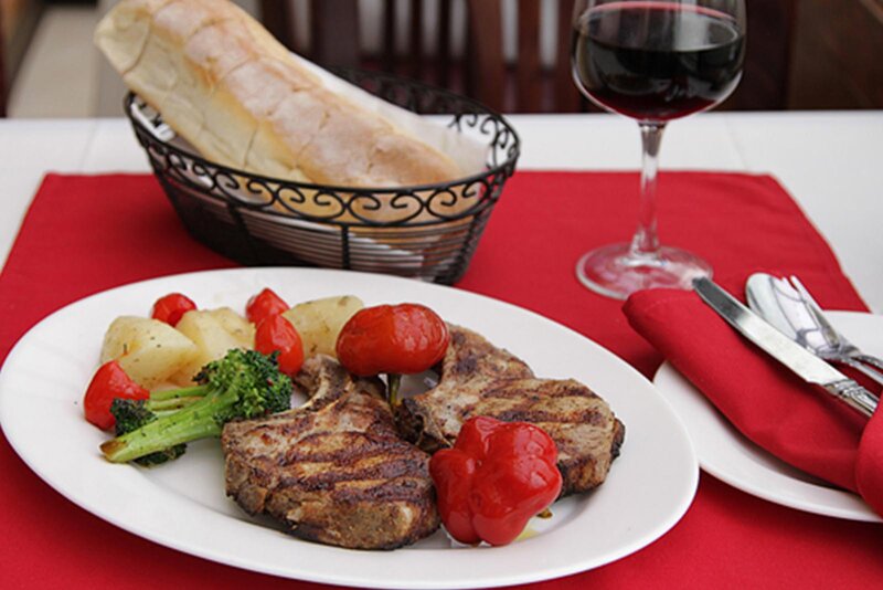 Steak entree with sauteed vegetables with a basket of bread and a glass of red wine